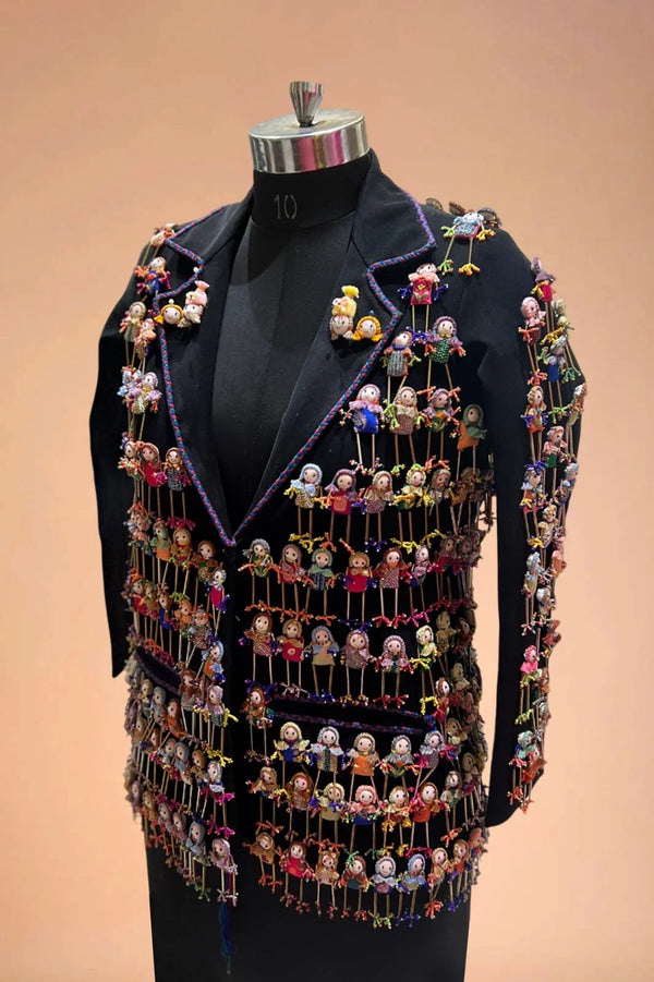 Black blazer adorned with colorful handcrafted doll embellishments on a mannequin.