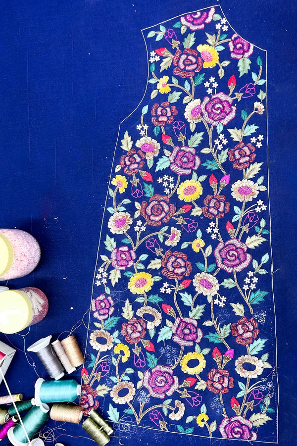 Handcrafted navy blue fabric piece with vibrant floral embroidery, threads and beads nearby