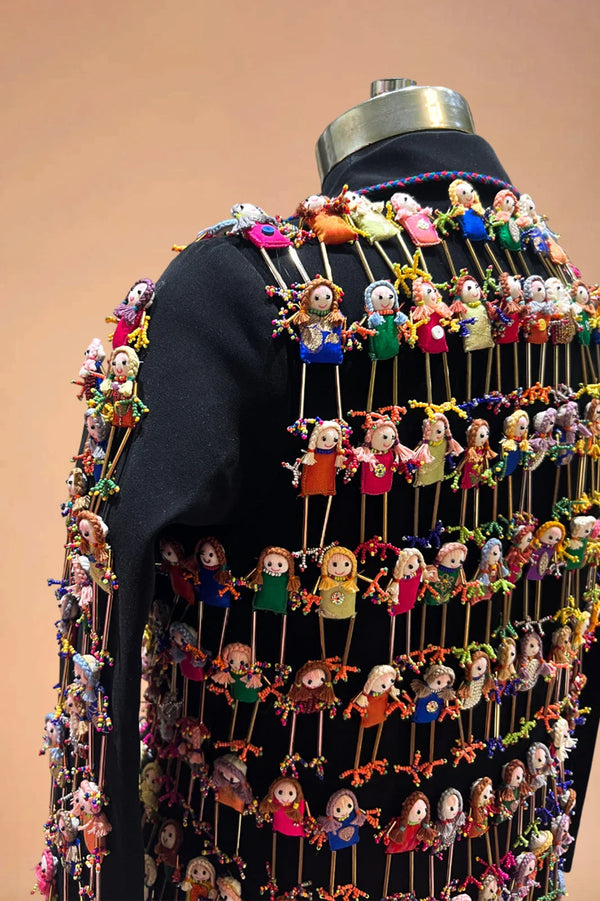 Black blazer adorned with rows of colorful handcrafted doll embellishments, displayed on mannequin