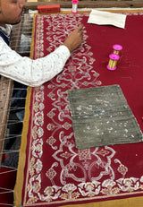 Artisan hand-embroidering a maroon pashmina shawl with intricate floral patterns