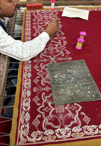 Artisan hand-embroidering a maroon pashmina shawl with intricate floral patterns