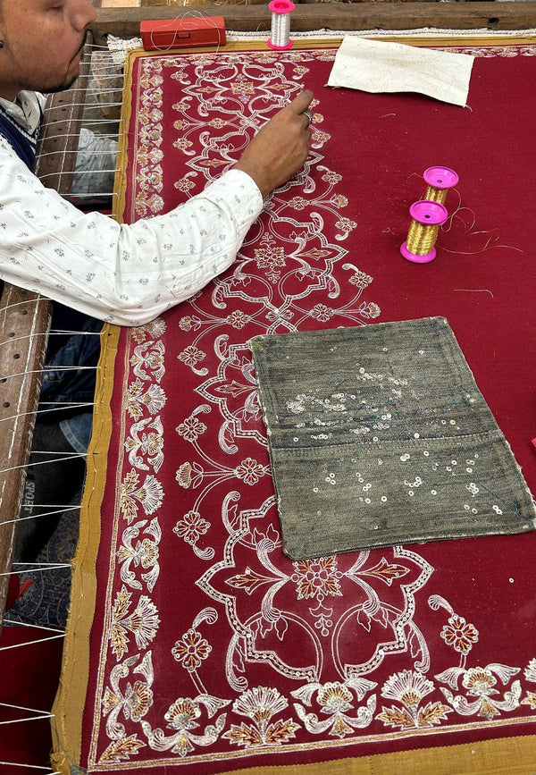 Artisan hand-embroidering a maroon pashmina shawl with intricate floral patterns