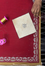 Artisan hand-embroidering a red pashmina shawl with gold thread and floral border