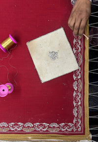 Artisan hand-embroidering a red pashmina shawl with gold thread and floral border
