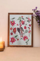 Framed wall art with colorful embroidered bird, floral motifs and leaves on a light background