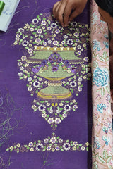 Handcrafted floral embroidery in green, purple, and white on purple fabric, artisan at work