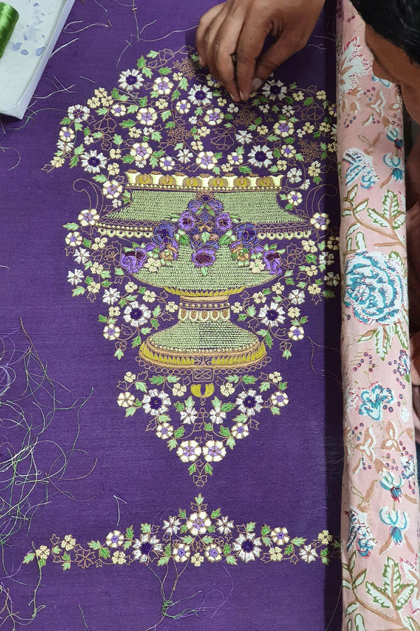 Handcrafted floral embroidery in green, purple, and white on purple fabric, artisan at work