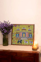 Embroidered Indian palace wall art with floral designs, elephants, and horses on a table next to purple flowers and candles.