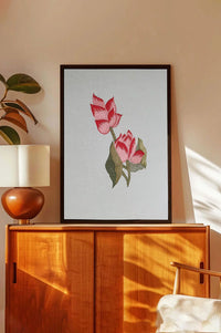 Framed botanical wall art with pink flowers and green leaves above a wooden cabinet in a sunlit room