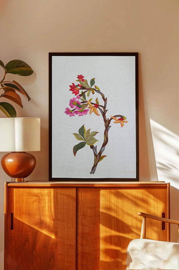 Framed wall art of a colorful floral branch on a white background above a wooden sideboard