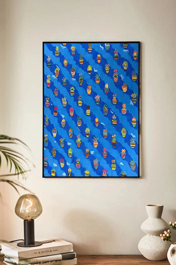 Framed artwork with a blue background and colorful pattern on a wall above a shelf.